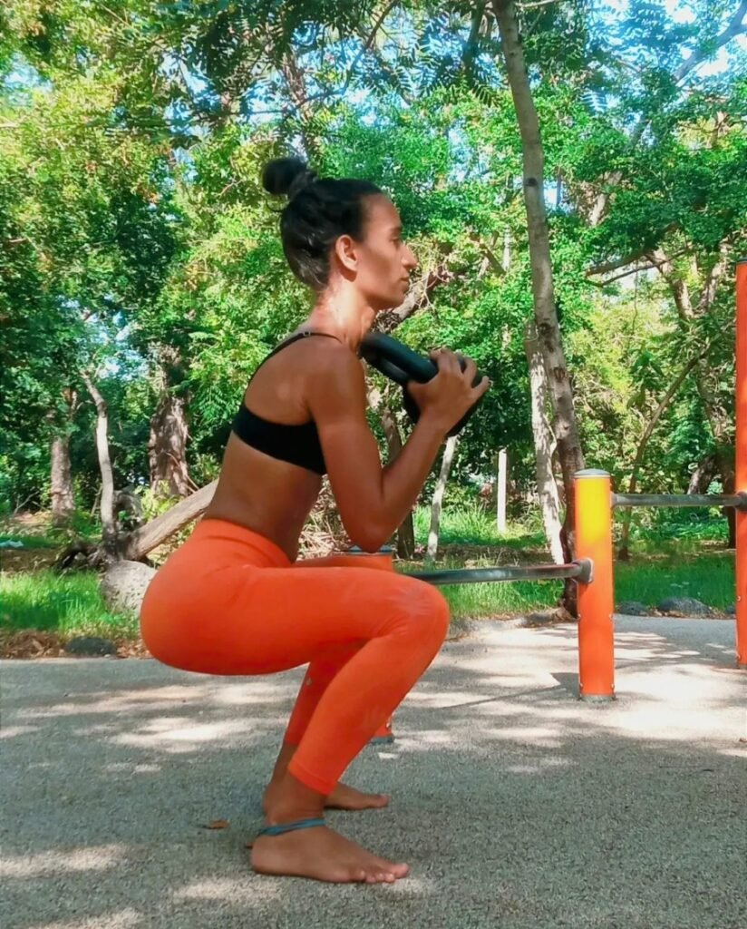client réalisant un exercice de musculation au kettlebell en extérieur à la réunion accompagnéé par un coach sportif